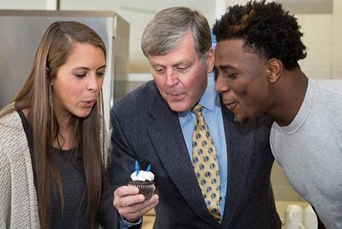 T.Haas and two GVSU students blowing out a candle on a cupcake